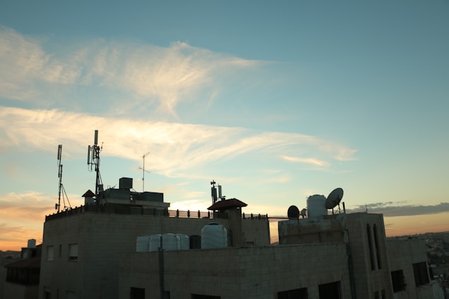 A technician installing a wireless antenna on a rooftop overlooking Balkh's landscape at sunset.