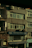 A multi-story building with various business signage, including one that reads 'Taksim Büro Kırtasiye.' The facade shows multiple windows and a few air conditioning units attached to the exterior. The building's exterior appears slightly worn, and some balconies and old metal railings are visible. The overall scene is dimly lit, probably captured during early morning or late afternoon.