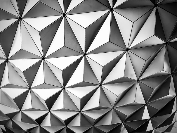 Geometric pattern with repeating triangles and diamond shapes, creating a tessellation in shades of gray.