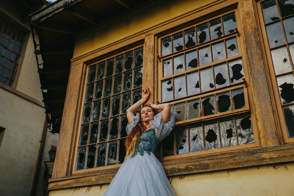 a woman in a blue dress standing in front of a window