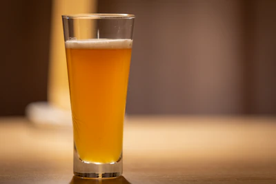 Close-up of a hand holding a tulip glass filled with amber beer, highlighting the foam and clarity.