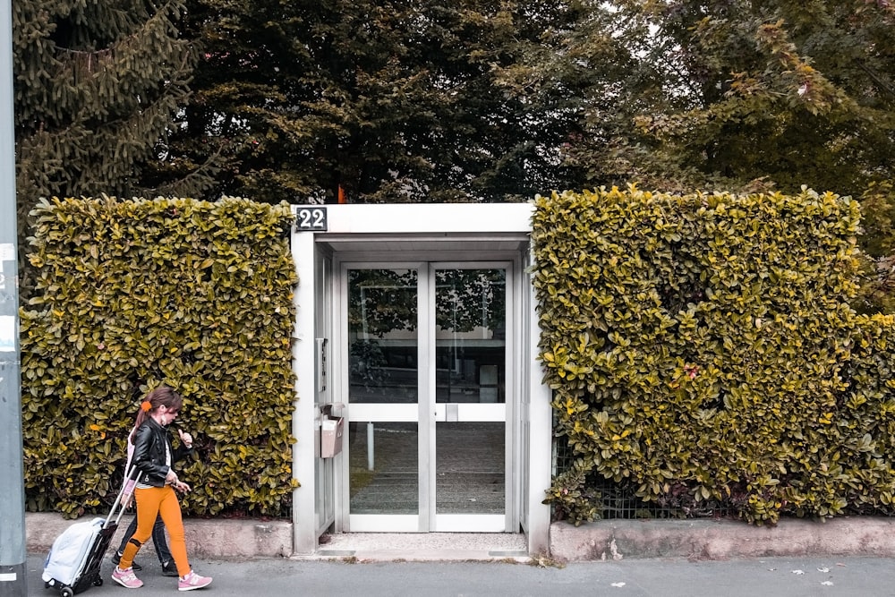 a woman walking down a street past a tall hedge