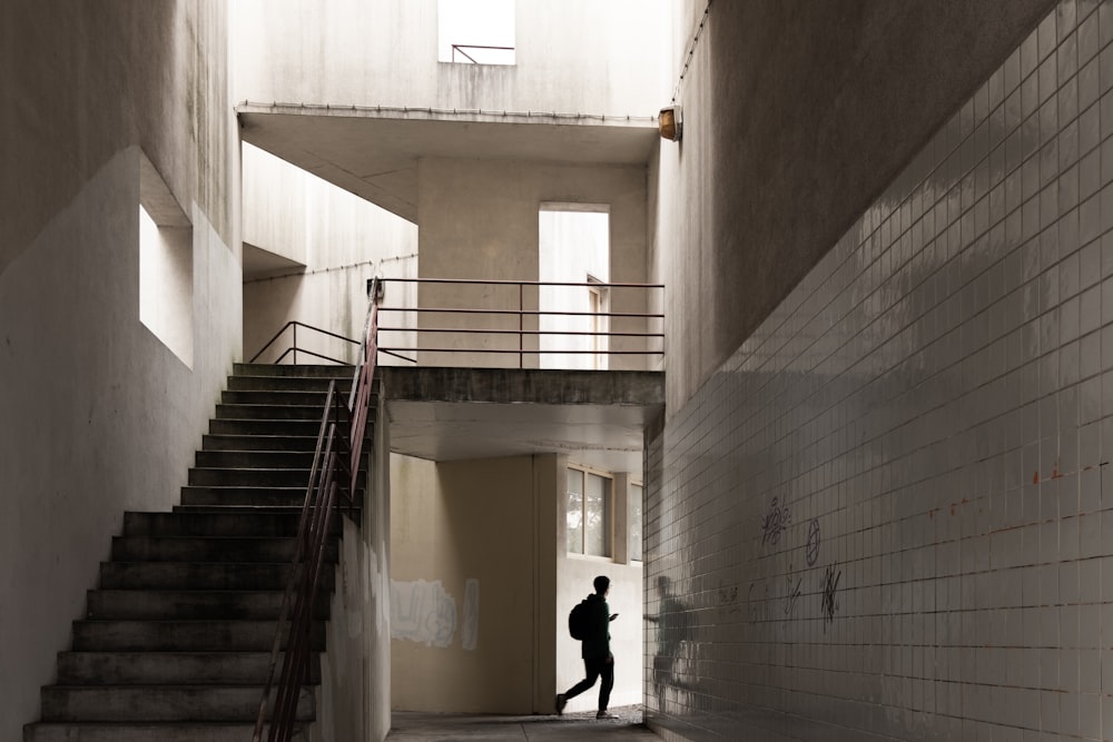 a man walking down a hallway next to a set of stairs