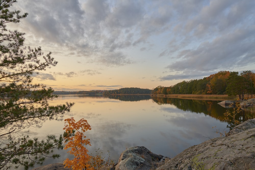 a lake surrounded by rocks and trees with a sunset in the background