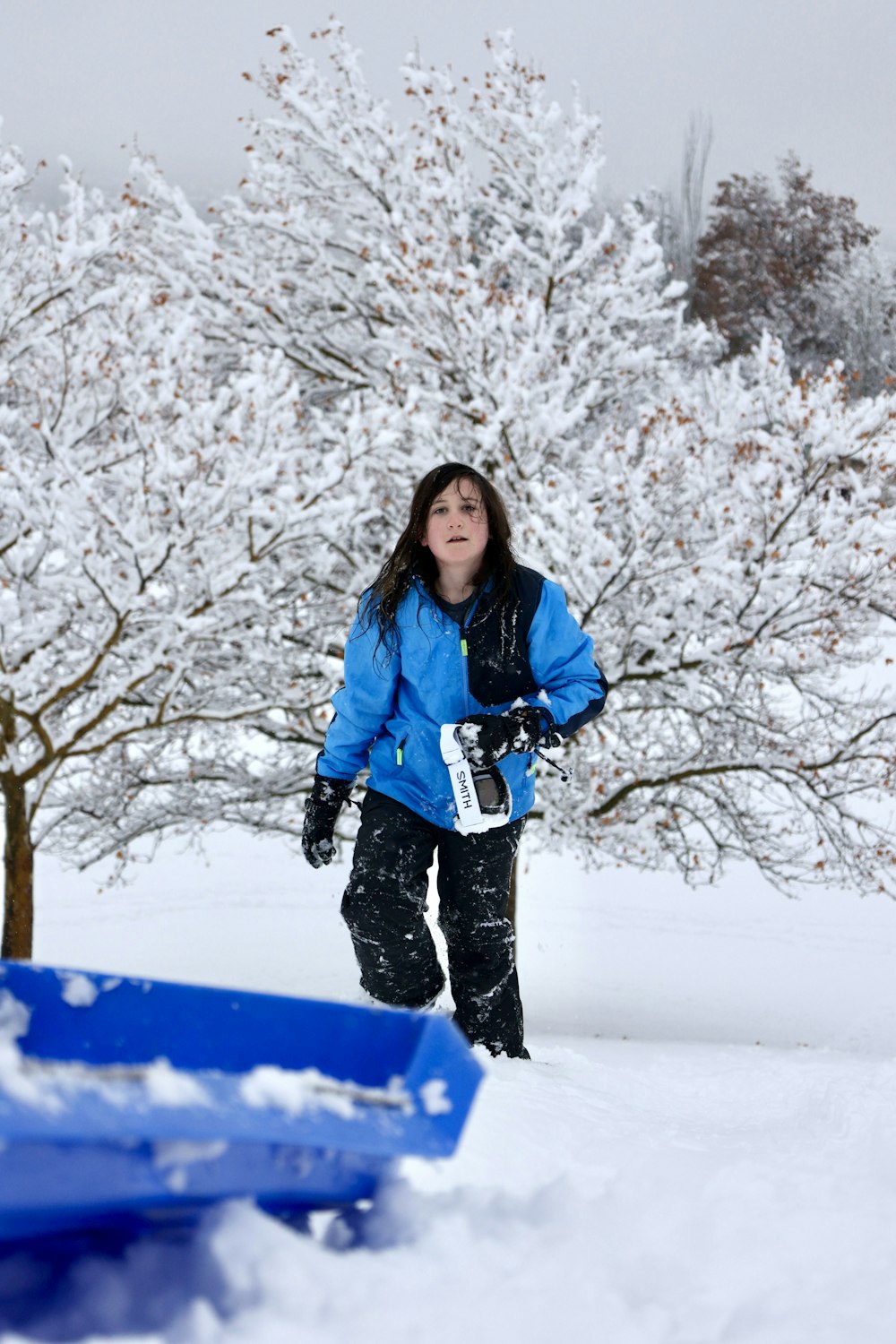 a young girl standing in the snow with a snowboard