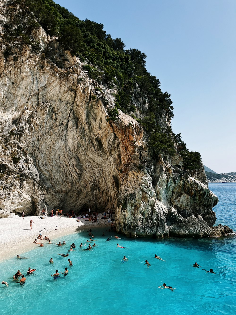 a group of people swimming in the ocean next to a cliff