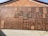 A large wall display featuring an array of wooden plaques with Chinese characters engraved on them. The plaques vary in size and are arranged in a seemingly random pattern against a backdrop of tiles. The bright sunlight casts shadows, highlighting the texture and depth of the engravings.