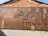 A large wall display featuring an array of wooden plaques with Chinese characters engraved on them. The plaques vary in size and are arranged in a seemingly random pattern against a backdrop of tiles. The bright sunlight casts shadows, highlighting the texture and depth of the engravings.