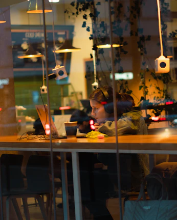 Student using a lightweight laptop on a cozy cafe table with headphones.