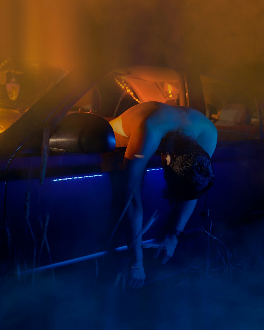 a naked woman leaning over a car in the dark