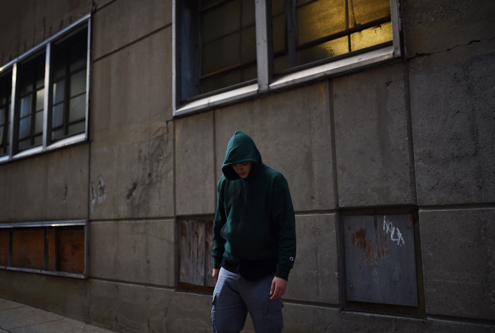 a man in a green hoodie walking down a sidewalk