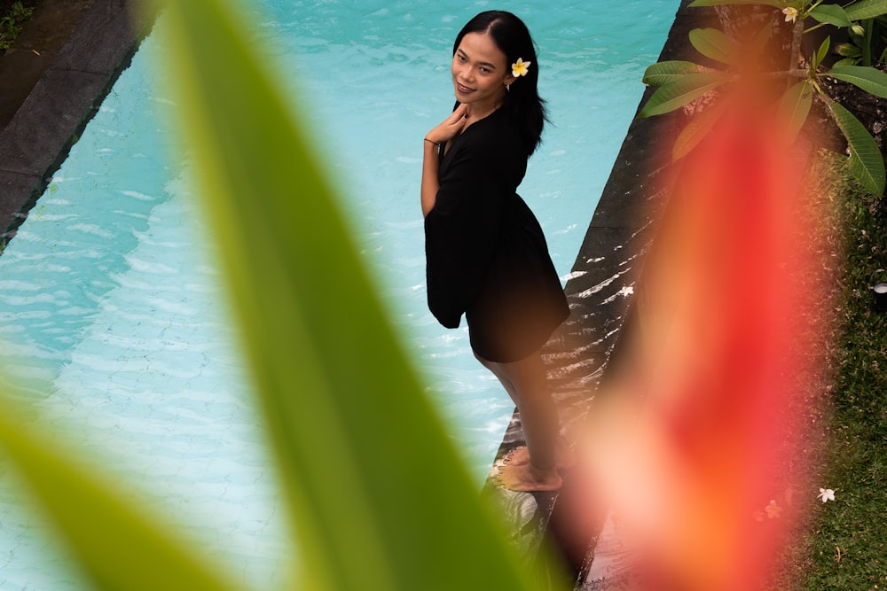 a woman in a black dress standing next to a pool