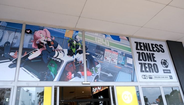 An animated promotional banner for Zenless Zone Zero features colorful characters and dynamic artwork displayed above glass doors. A pink-haired character with futuristic attire sits on a vehicle, while other animated figures appear around it. The banner includes bold text with the game’s title.