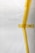 A white surface partially covered with strips of yellow masking tape arranged in an abstract pattern. There is a visible barcode on one piece of tape.