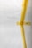 A white surface partially covered with strips of yellow masking tape arranged in an abstract pattern. There is a visible barcode on one piece of tape.
