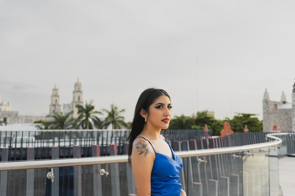 a woman in a blue dress standing in front of a fence