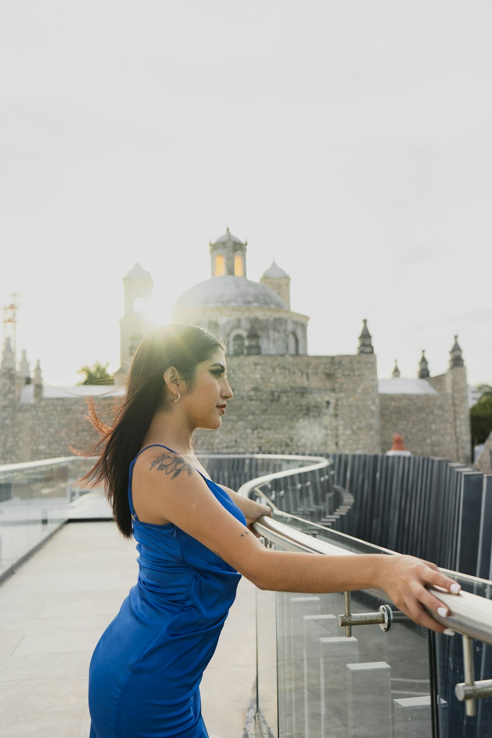 a woman in a blue dress leaning on a railing
