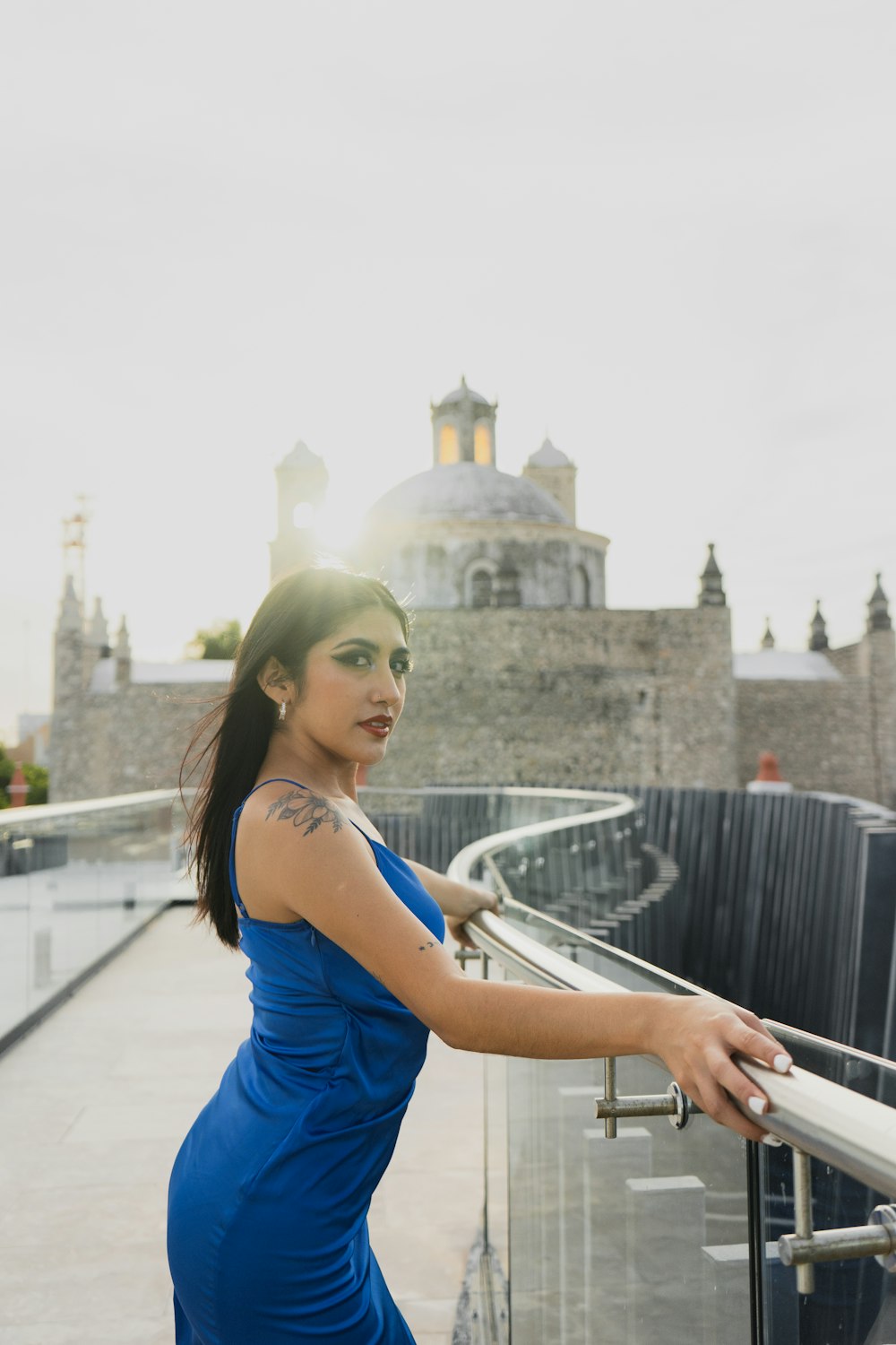 a woman in a blue dress leaning on a railing