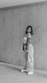 Black and white photo of a confident model leaning against a textured wall.