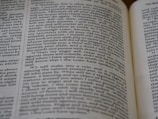 Close-up view of an open book, showing printed text across its pages. The words appear clear, with a focus on religious or biblical content.
