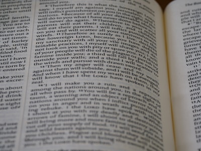 Close-up view of an open book, showing printed text across its pages. The words appear clear, with a focus on religious or biblical content.