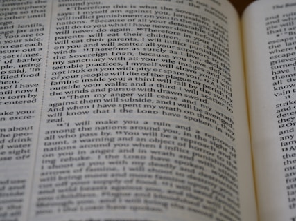 Close-up view of an open book, showing printed text across its pages. The words appear clear, with a focus on religious or biblical content.