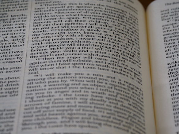 Close-up view of an open book, showing printed text across its pages. The words appear clear, with a focus on religious or biblical content.