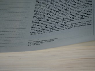 A close-up view of a page from an open book, displaying printed text in multiple paragraphs. The text is partially obscured by the page curvature. Margins contain dotted lines, and there are footnotes or annotations at the bottom of the page.