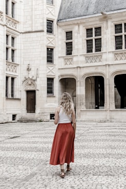 a woman in a red skirt is standing in front of a large building