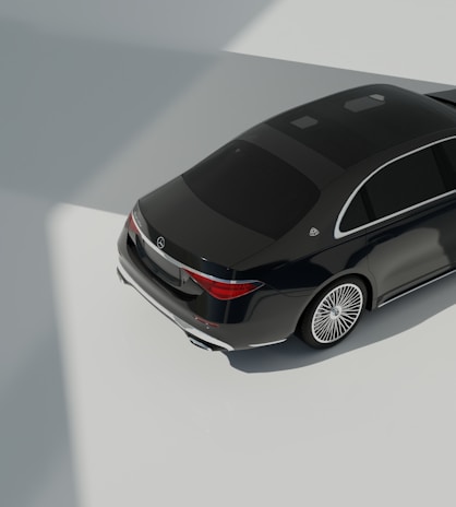 A dark luxury car is parked on a smooth, light-colored surface with clear reflections. The car features elegant design elements such as sleek curves and shiny metallic accents. The lighting creates strong shadows and highlights, suggesting an indoor environment with natural light coming from above.