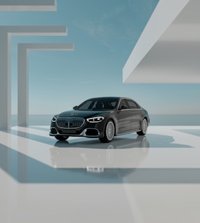 A sleek black luxury car is positioned in a modern, minimalistic architectural environment. The setting features geometric shapes and large, open spaces bathed in natural light. The sky is clear with subtle clouds, creating a serene backdrop. The car is prominently displayed, reflecting light off its polished surface.