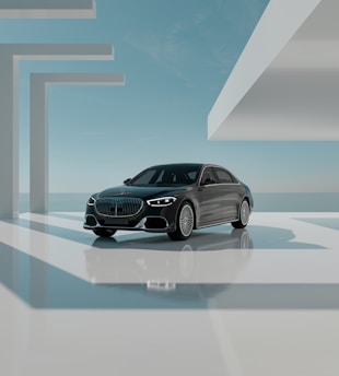 A sleek black luxury car is positioned in a modern, minimalistic architectural environment. The setting features geometric shapes and large, open spaces bathed in natural light. The sky is clear with subtle clouds, creating a serene backdrop. The car is prominently displayed, reflecting light off its polished surface.