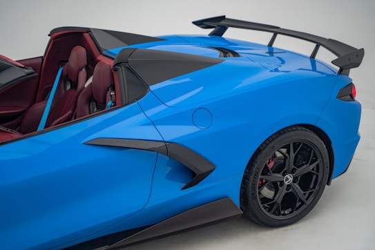A sleek, blue sports car showcasing its aerodynamic design with a prominent rear spoiler, black rims, and a vibrant red interior. The image emphasizes the car&rsquo;s modern and sporty aesthetic.