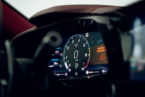 A close-up view of a digital car dashboard with a central speedometer displaying zero mph. The gauge is circular and surrounded by various indicators. There are warning lights and other textual information such as 'Key Missing' warning and 'Check for K' notification. The dashboard is sleek and modern, emphasizing technology and precision.