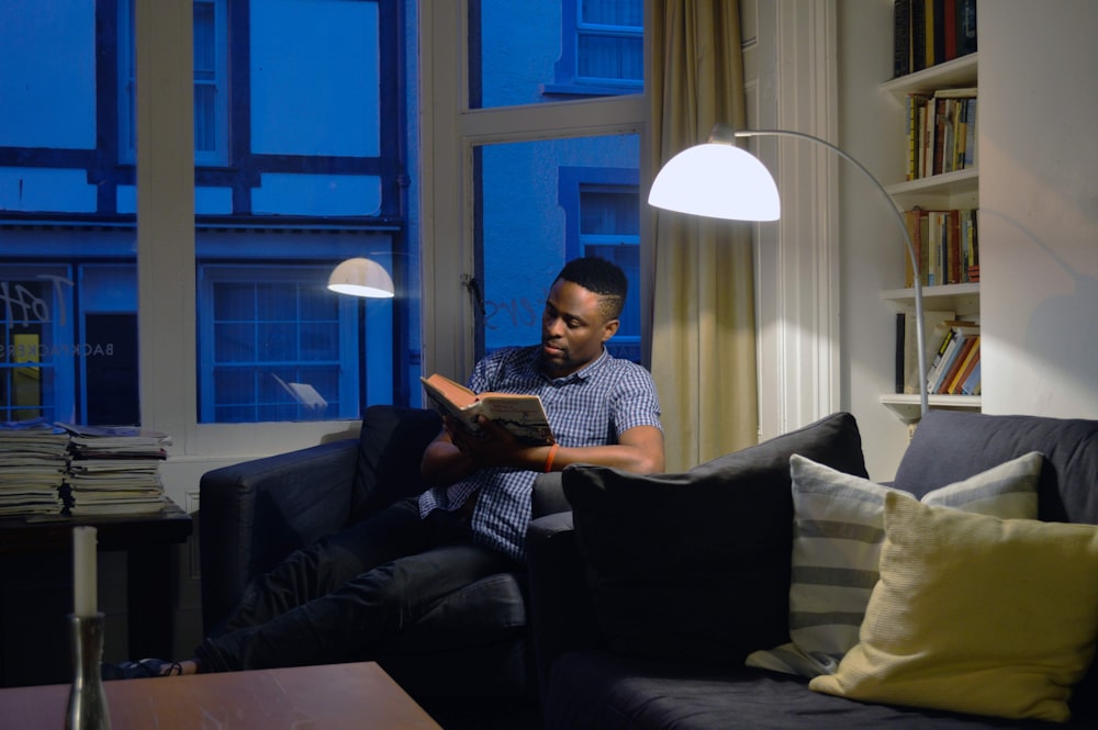 a man sitting on a couch reading a book