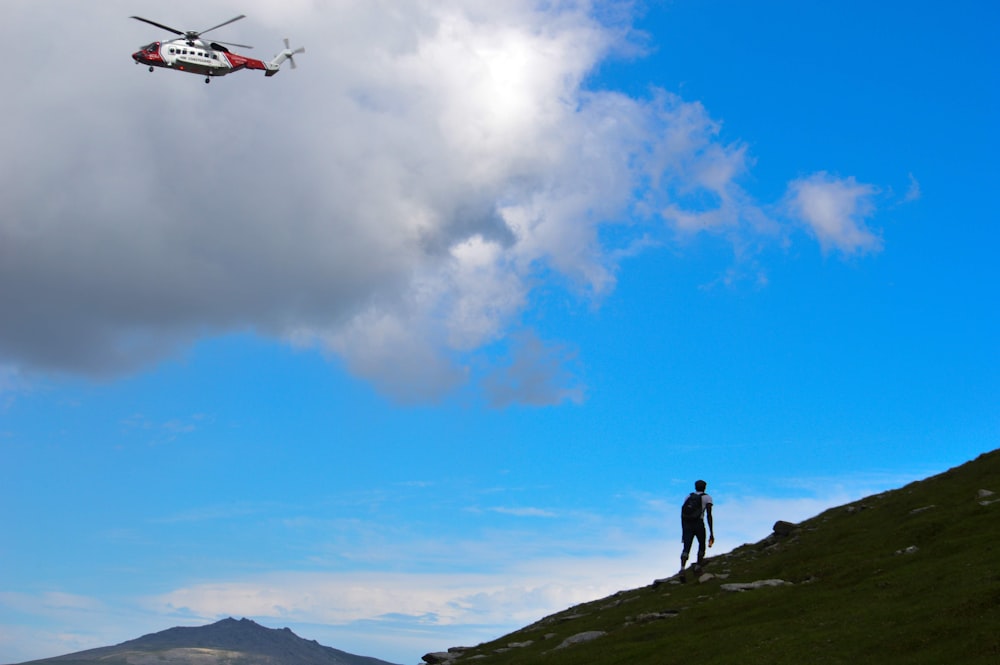 a helicopter flying over a man standing on top of a hill