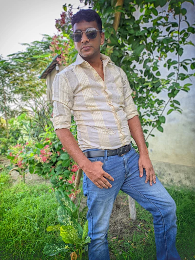 A relaxed model wearing a soft cotton shirt and jeans, standing in a sunlit urban park.
