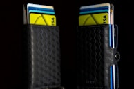 Two black wallets with a geometric hexagonal pattern are filled with colorful credit and bank cards sticking out. The wallets are positioned against a dark background, making the vivid colors of the cards—yellow, blue, and white—stand out prominently.