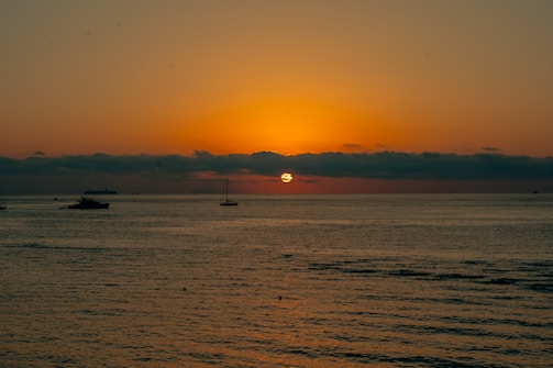 a sunset over the ocean with boats in the water