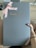A large box with a sleek, matte gray surface features the embossed gold logo 'house cb London' at the center. A pink ribbon tied into a bow decorates the top left corner, adding an elegant touch. A hand is holding the box against a light wood floor background.
