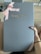 A large box with a sleek, matte gray surface features the embossed gold logo 'house cb London' at the center. A pink ribbon tied into a bow decorates the top left corner, adding an elegant touch. A hand is holding the box against a light wood floor background.