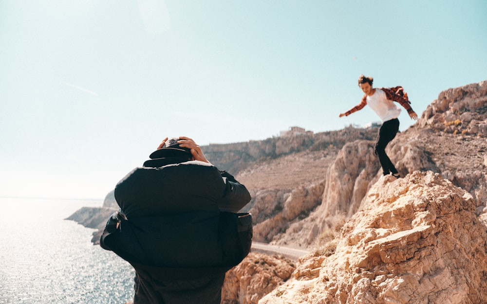 a man taking a picture of a man jumping off a cliff