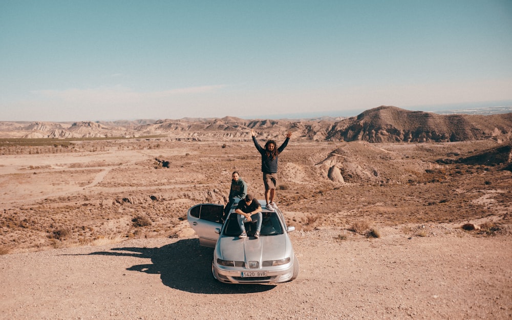 two people standing on top of a car in the desert