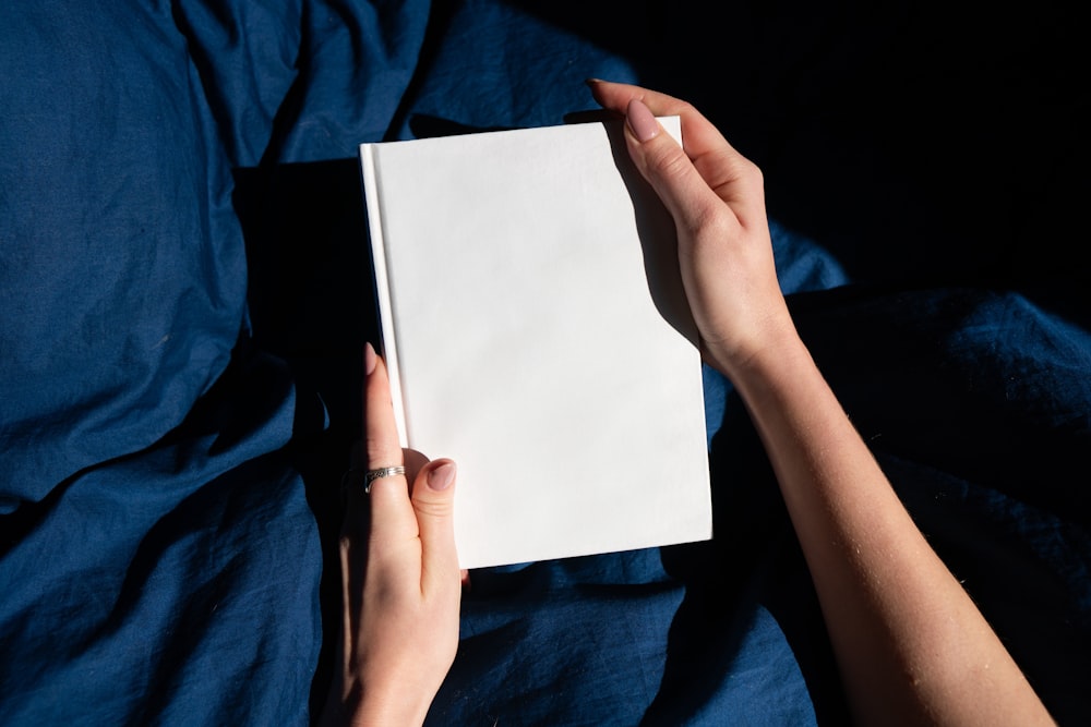 a person is holding a book on a bed