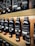 Multiple bottles of fragrance oil are neatly arranged on wooden shelves. The bottles vary in size and have labels with text both in English and another language. The lighting is warm, highlighting the sleek, dark-colored containers.