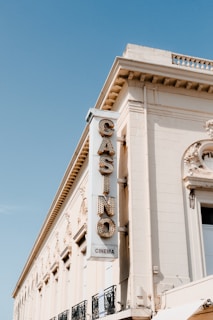 A vintage building features a vertical sign with the word 'CASINO' in large, lit letters, and 'CINEMA' below. The architecture includes ornate detailing near the roofline, and the facade has a cream color. The sky is clear and blue, enhancing the nostalgic feel of the setting.