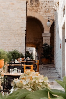 A cozy Italian café terrace bathed in warm afternoon light with rustic stone walls and vibrant flower pots.