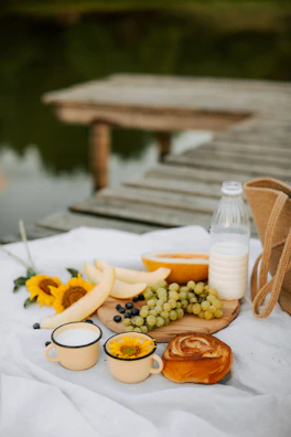 A close-up of a southern-style picnic setup with mason jars, fresh fruit, and a gingham cloth on a wooden table.