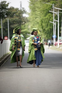 two women in graduation gowns walking down a street