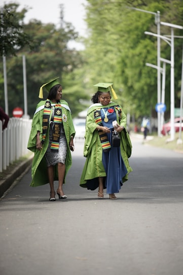 two women in graduation gowns walking down a street